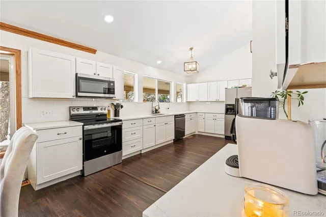 a kitchen with stainless steel appliances white cabinets a sink a stove a microwave and wooden floors