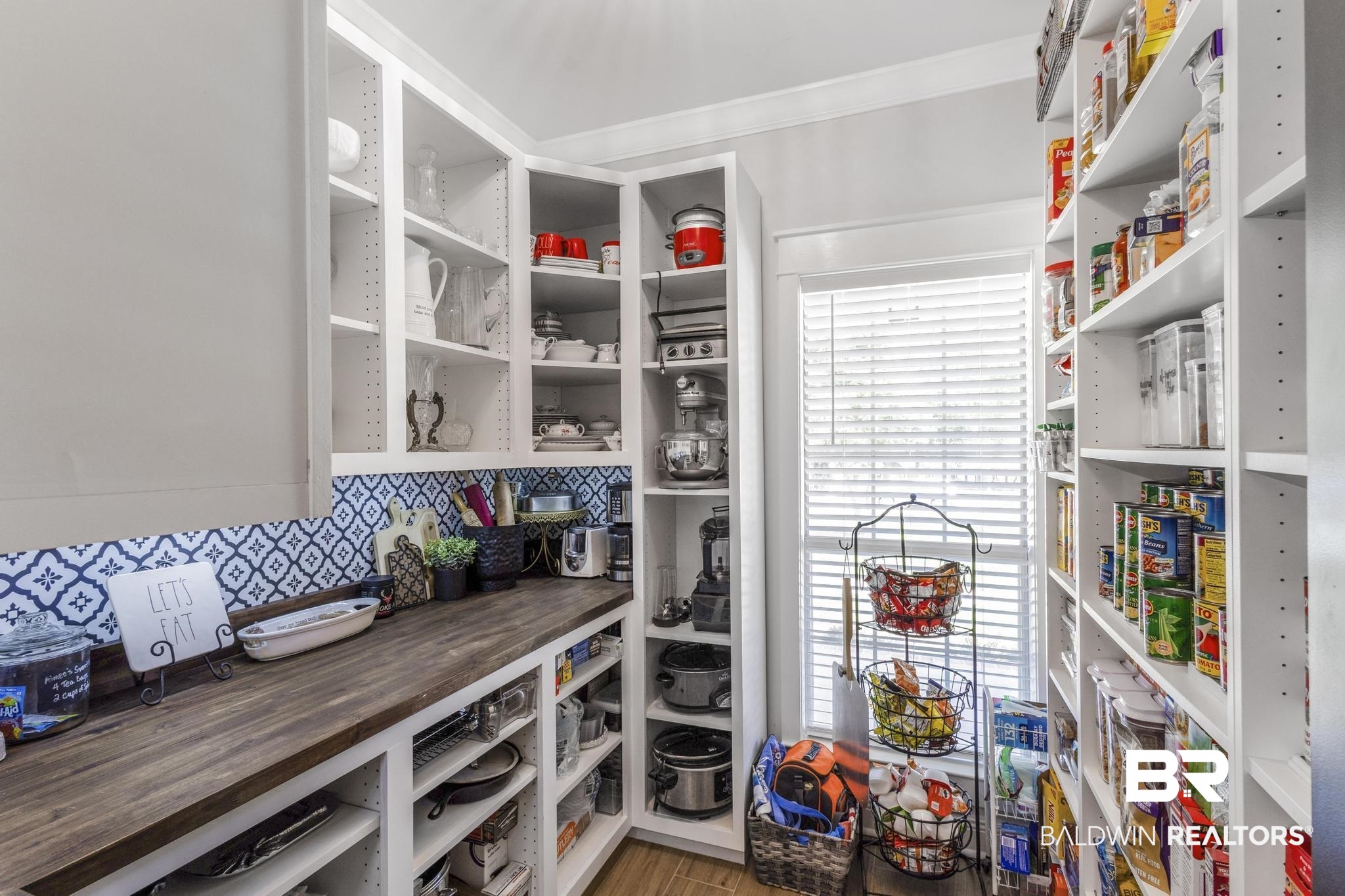 83 Caisson Trace Daphne, AL 36527 - Photo 26 of 63 Corner pantry featuring extensive open shelving, a spacious wood-finish countertop, decorative blue and white patterned tile backsplash, and natural light from a window with blinds