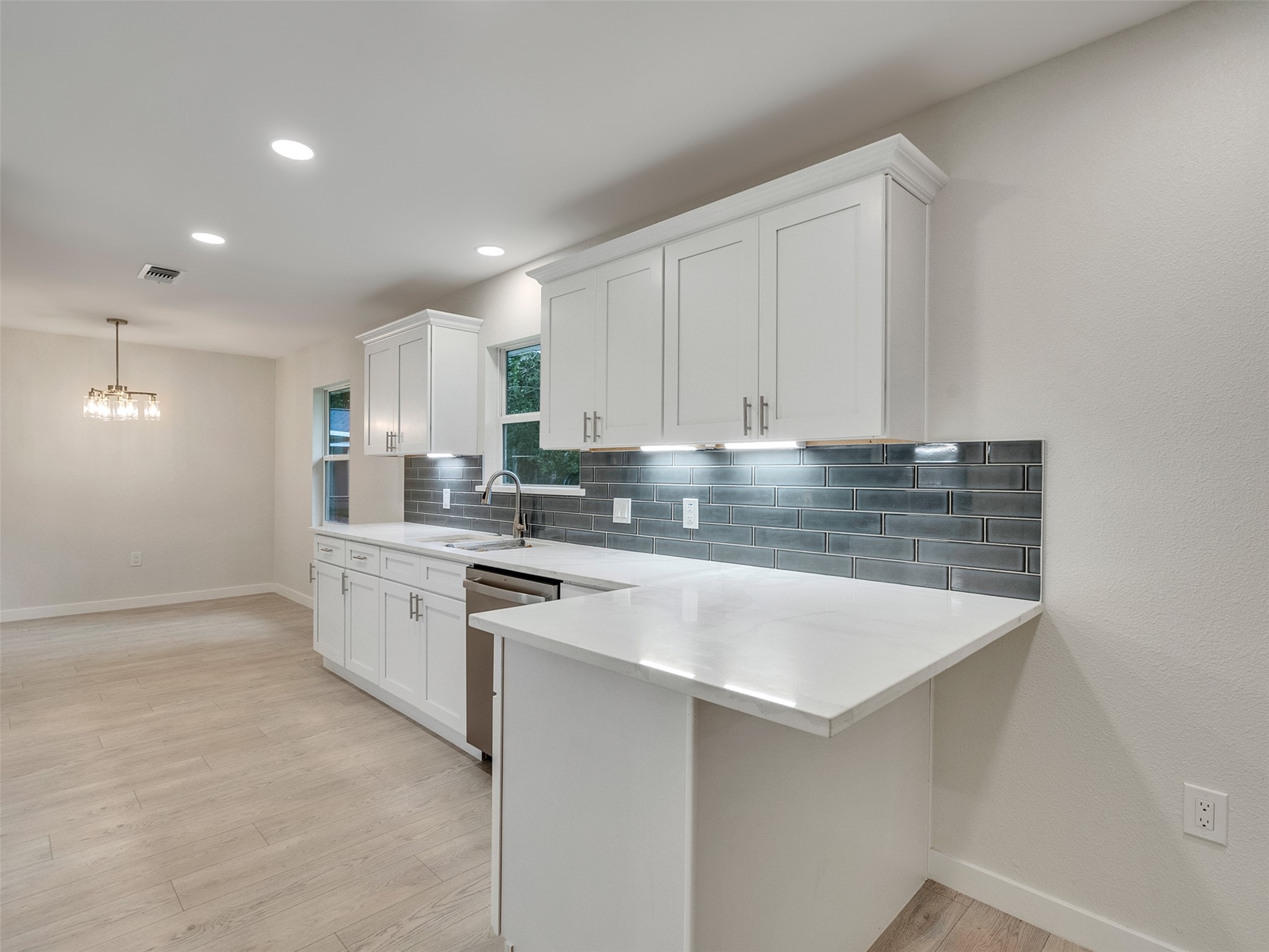 10315 Winding Trail Road La Porte, TX 77571 - Photo 9 of 24 This modern kitchen features sleek white cabinetry, elegant blue/gray tile backsplash, and a cozy breakfast bar for two, perfect for intimate morning meals.
