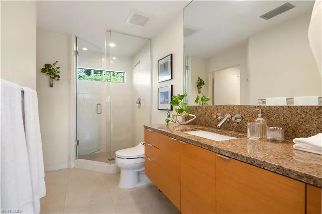 a bathroom with a granite countertop sink a toilet a mirror and shower