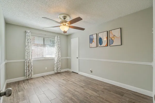 an empty room with wooden floor chandelier fan and windows
