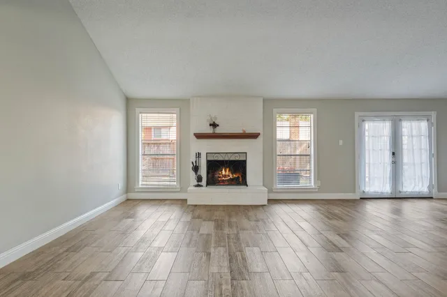 a view of an empty room with wooden floor windows and a fireplace