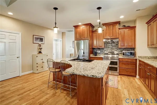 a kitchen with stainless steel appliances kitchen island granite countertop a stove a sink dishwasher and white cabinets with wooden floor
