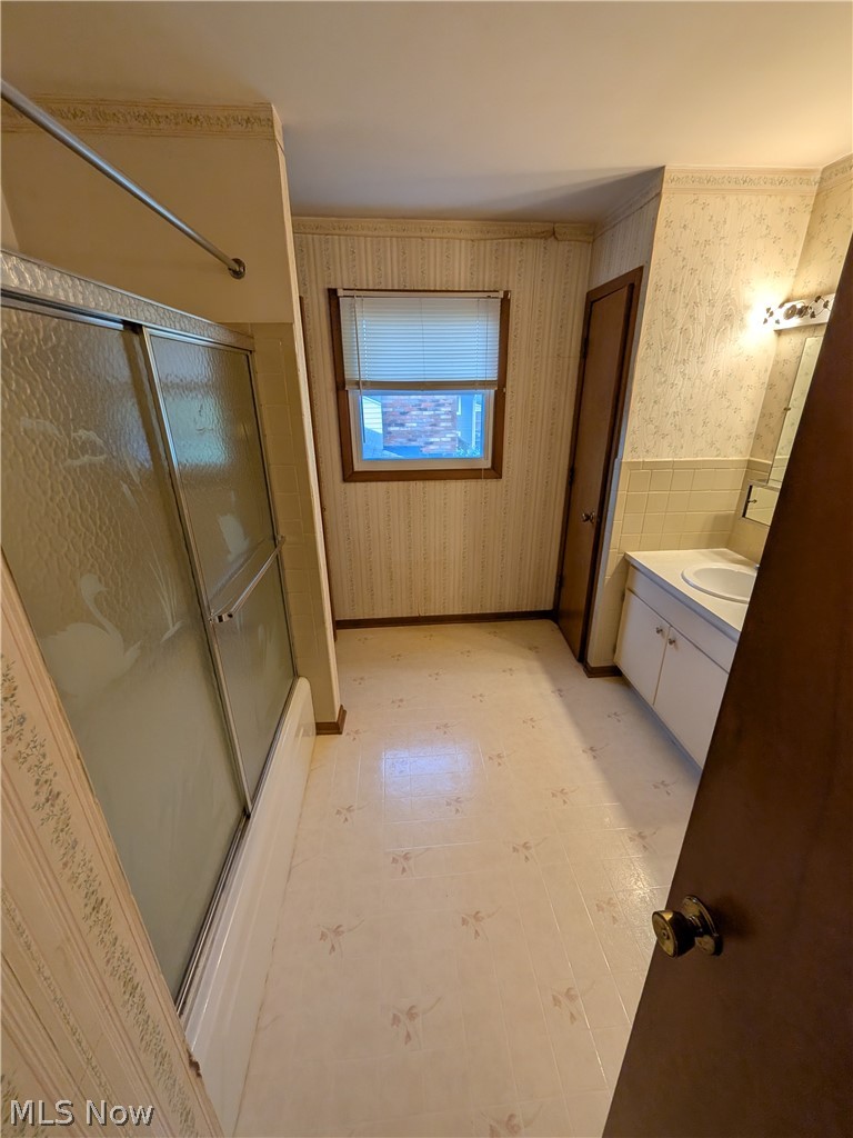 1161 Gulf Road Elyria, OH 44035 - Photo 21 of 34 Bathroom featuring a shower-tub combination with sliding glass doors, a single window, vanity with a rectangular sink, and patterned flooring
