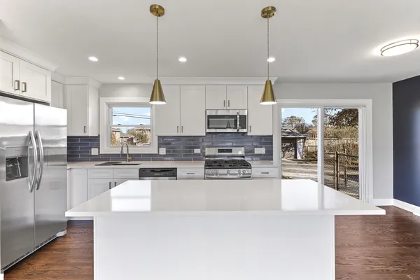 a kitchen with stainless steel appliances kitchen island granite countertop a stove a sink a refrigerator a center island a stove and white cabinets with wooden floor