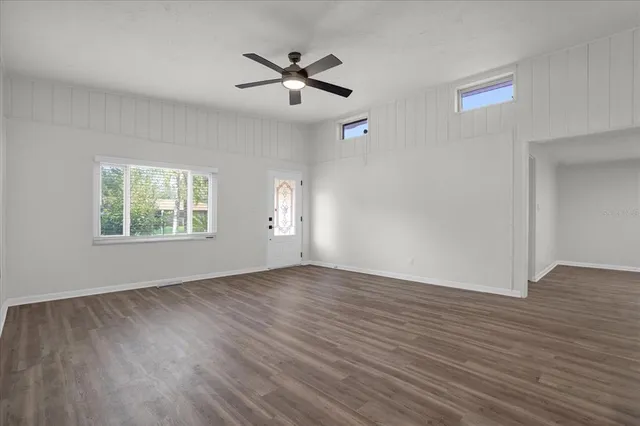 an empty room with wooden floor chandelier fan and windows