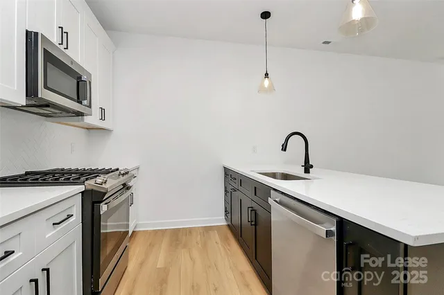 a kitchen with stainless steel appliances granite countertop a sink a stove top oven and wooden floor