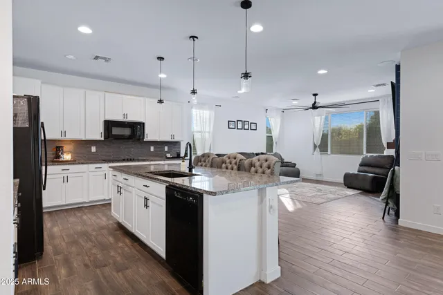 a large kitchen with stainless steel appliances kitchen island granite countertop a stove a sink a refrigerator and white cabinets with wooden floor