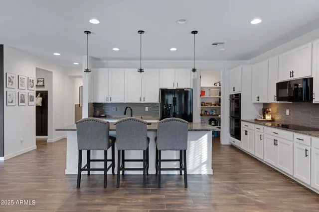 a kitchen with stainless steel appliances granite countertop a stove top oven a refrigerator a sink and a dining table with wooden floor