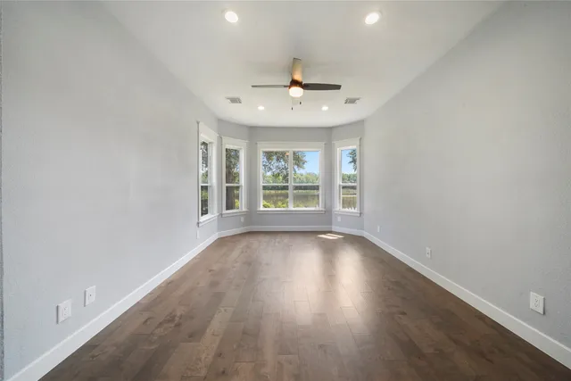 an empty room with wooden floor a ceiling fan and windows