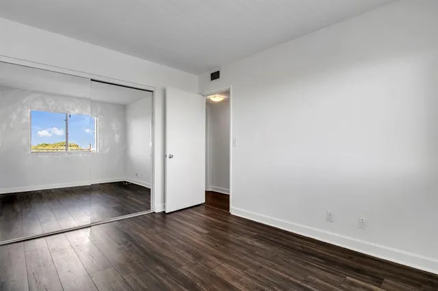 an empty room with wooden floor mirror and windows