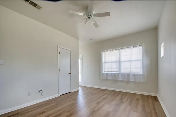 an empty room with wooden floor chandelier fan and windows