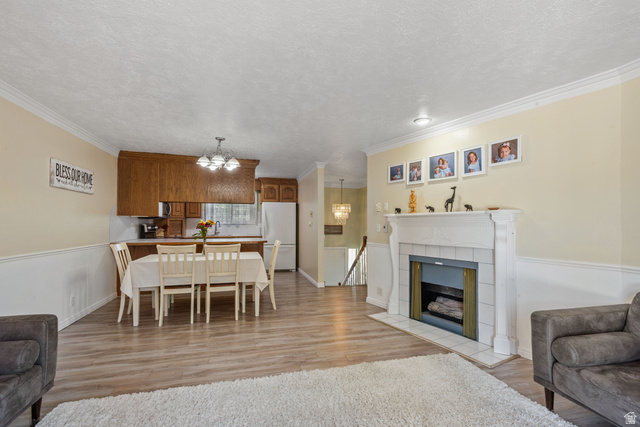 553 North 200 West Bountiful, UT 84010 - Photo 3 of 26 Dining area featuring light wood-style floors, a tile fireplace, hanging lights, crown molding, and a textured ceiling