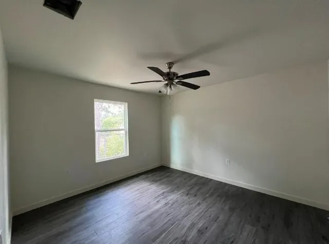 an empty room with wooden floor fan and windows