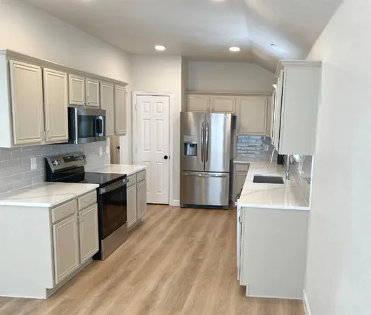 a kitchen with a sink a refrigerator and a stove top oven with wooden floor