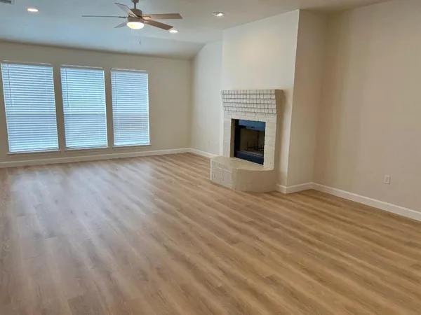 an empty room with wooden floor fireplace and windows