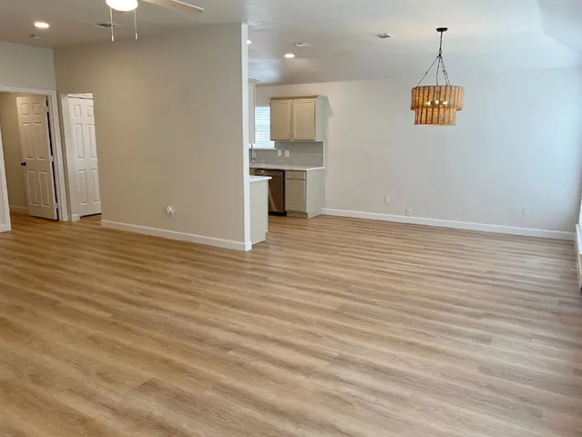 an empty room with wooden floor and kitchen view
