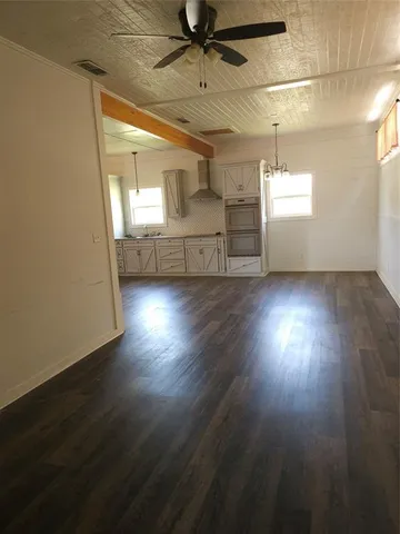 an empty room with wooden floor chandelier and windows