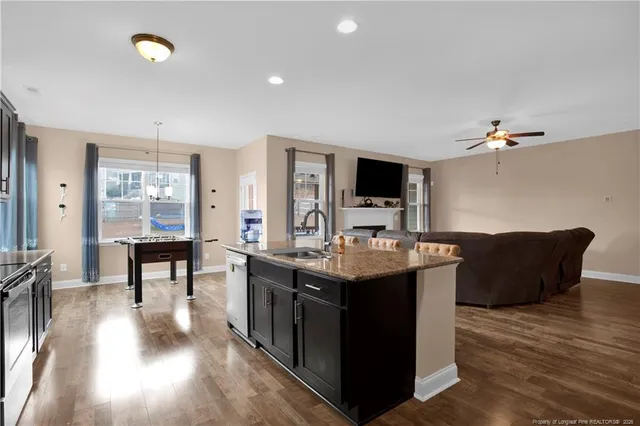 a living room with stainless steel appliances kitchen island granite countertop a table chairs and a wooden floor