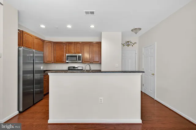 a kitchen with stainless steel appliances granite countertop a refrigerator a stove and a sink with wooden floor