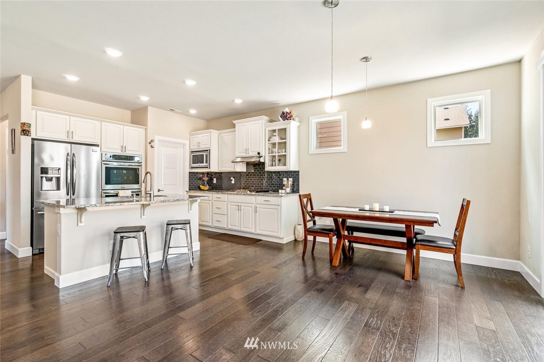 3919 176th Street Southeast Bothell, WA 98012 - Photo 8 of 31 a kitchen with stainless steel appliances kitchen island granite countertop a refrigerator a stove a sink a dining table and chairs with wooden floor