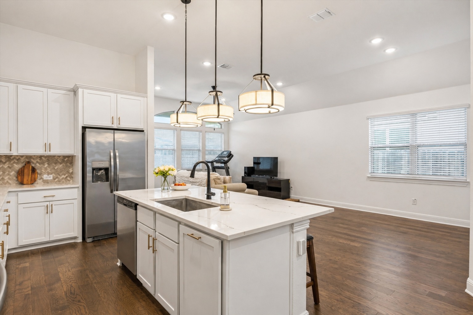 209 Rainier Drive Kyle, TX 78640 - Photo 11 of 24 Open-concept kitchen featuring an island with a built-in sink and three pendant lights, white cabinetry, stainless steel appliances, and wood-finish flooring
