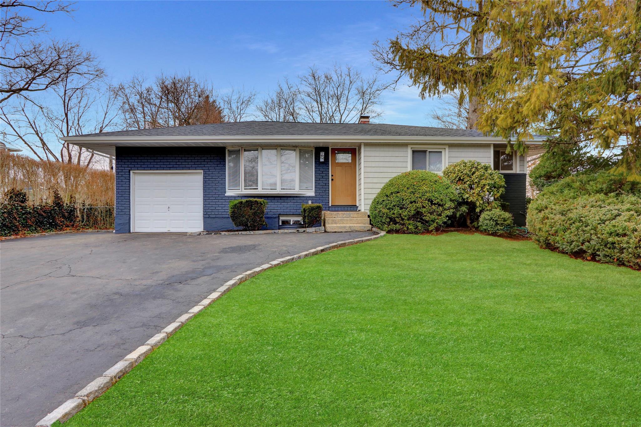 Ranch-style home featuring a chimney, a front lawn, a garage, aphalt driveway, and brick siding