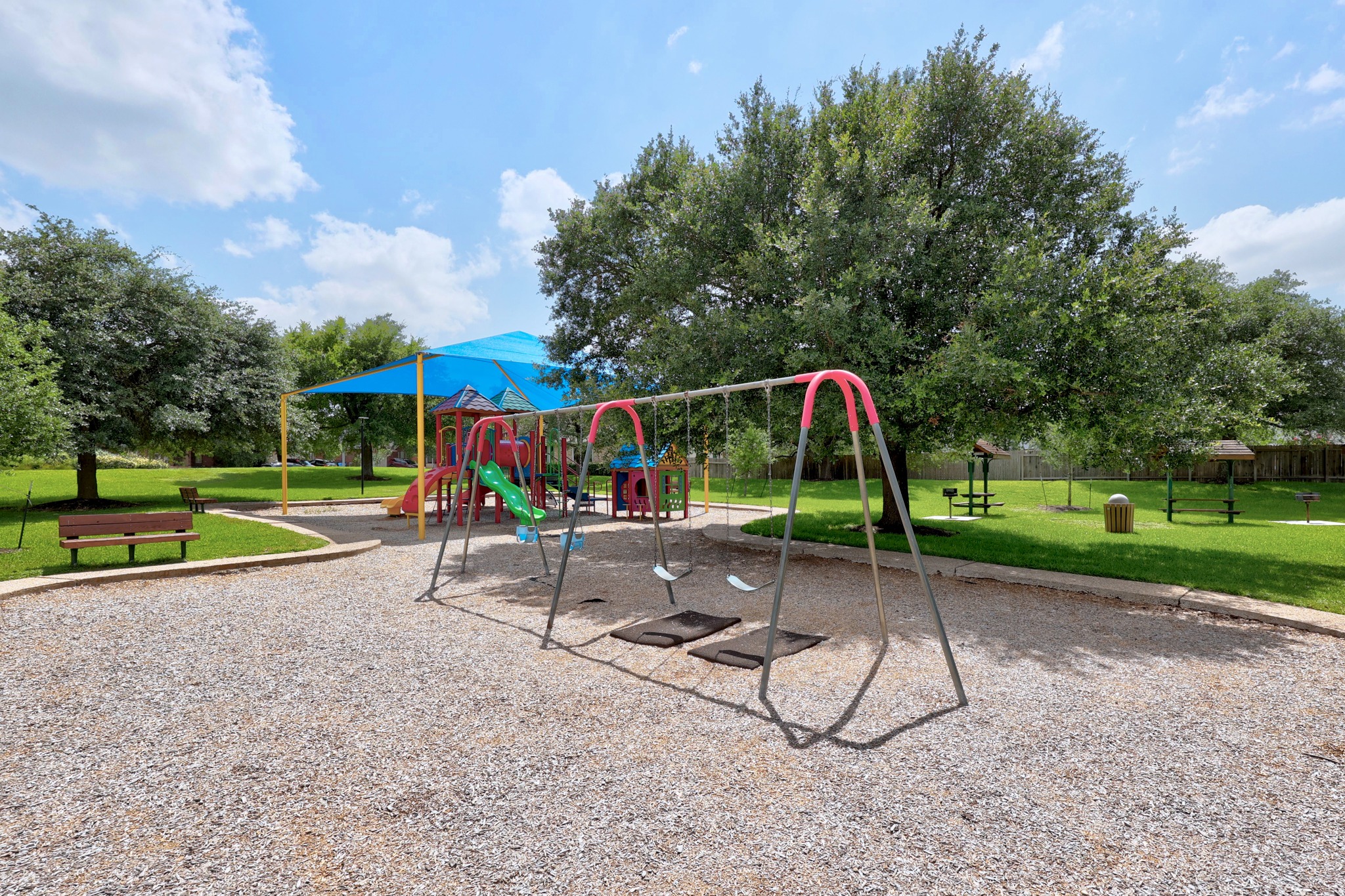 1108 Springbrook Road Pflugerville, TX 78660 - Photo 34 of 37 A vibrant playground set amidst verdant trees offers swings and play structures under a bright blue sky.