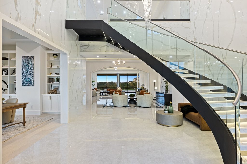 Grand entryway with a sleek, curved staircase and soaring ceilings leads to an inviting living area with scenic views.
