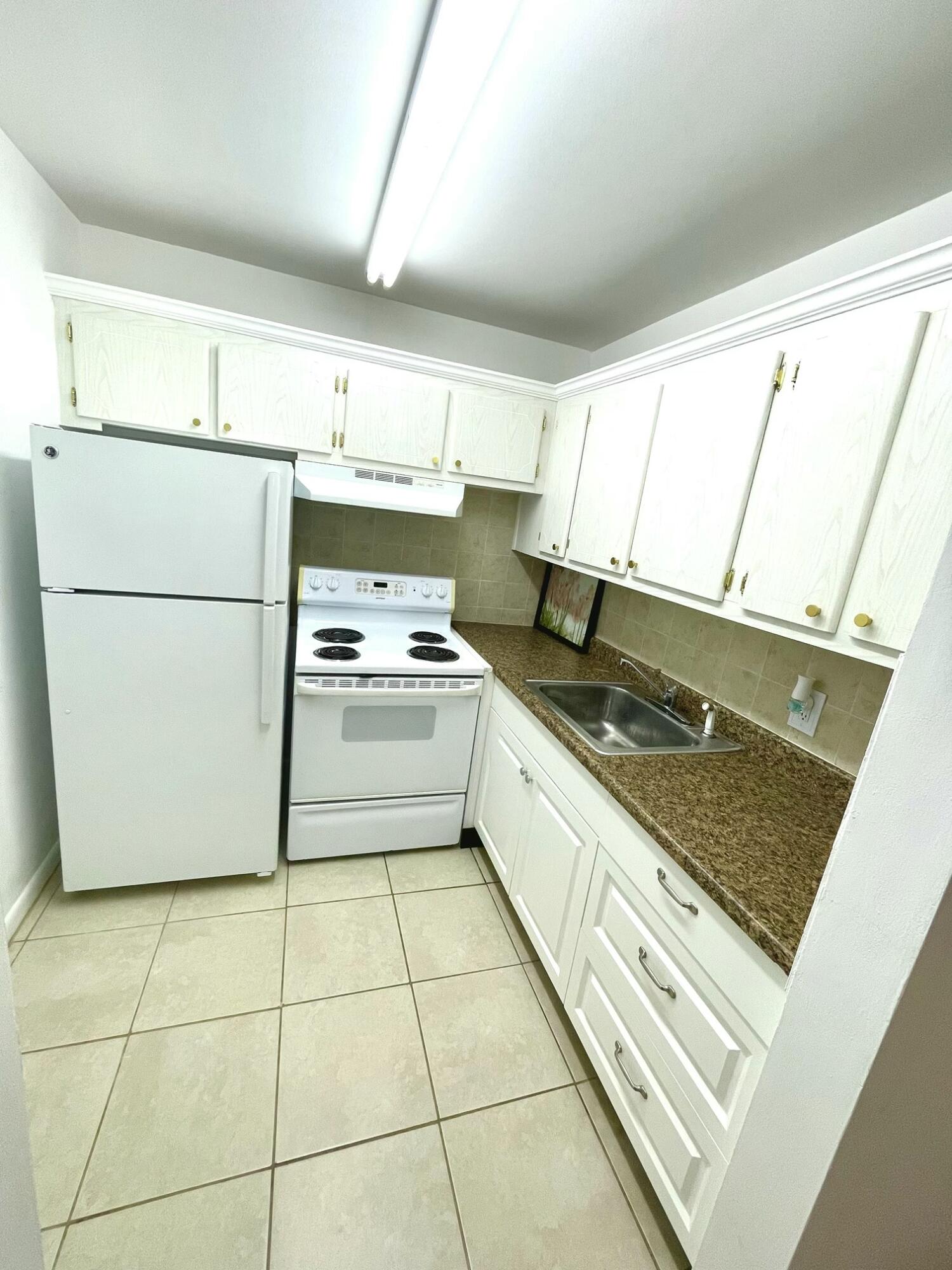128 Canterbury F, Unit 128 West Palm Beach, FL 33417 - Photo 2 of 17 a kitchen with a refrigerator a stove a sink and a window
