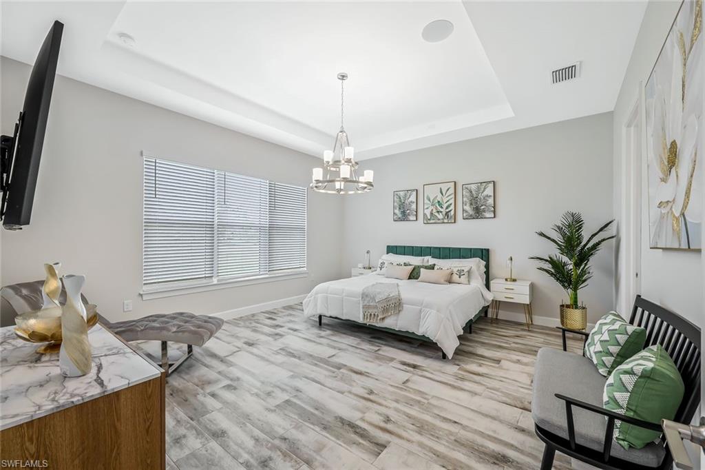 15495 Rio Ponace Court Naples, FL 34114 - Photo 11 of 43 Bedroom with a chandelier, a tray ceiling, and light wood-style floors