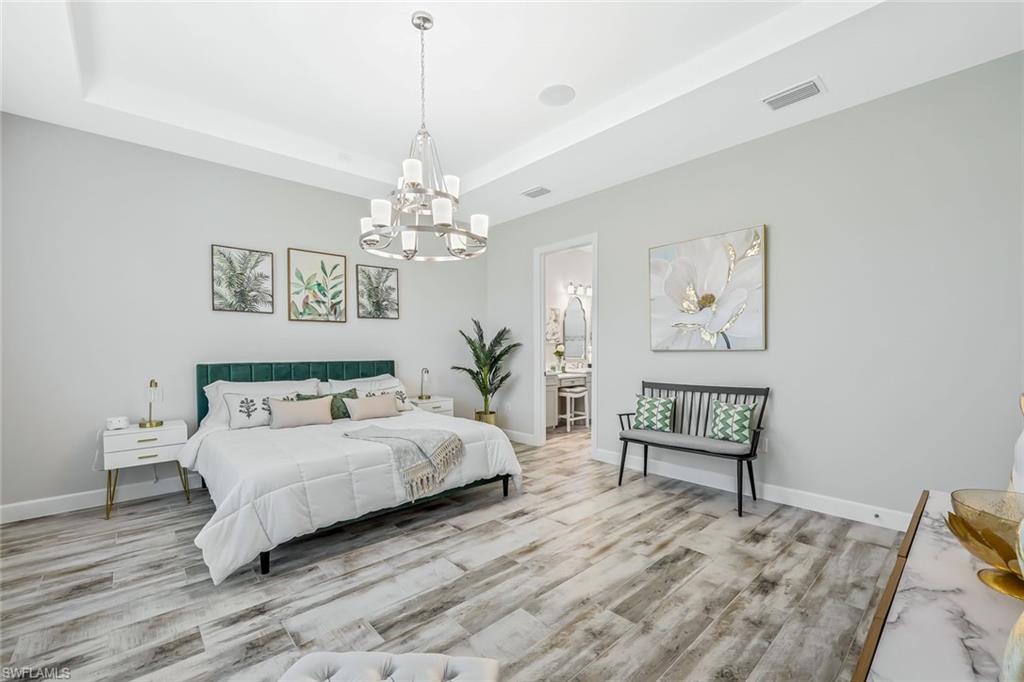 15495 Rio Ponace Court Naples, FL 34114 - Photo 12 of 43 Bedroom featuring a chandelier, a raised ceiling, wood finished floors, and ensuite bath