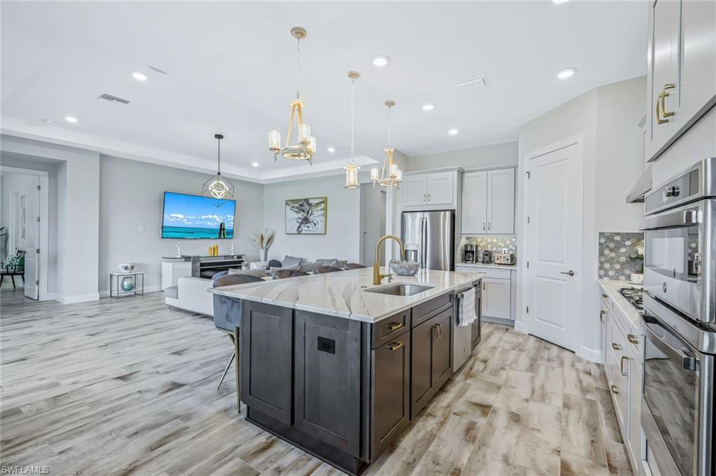 15495 Rio Ponace Court Naples, FL 34114 - Photo 8 of 43 Kitchen with stainless steel appliances, a chandelier, tasteful backsplash, light wood-type flooring, and recessed lighting