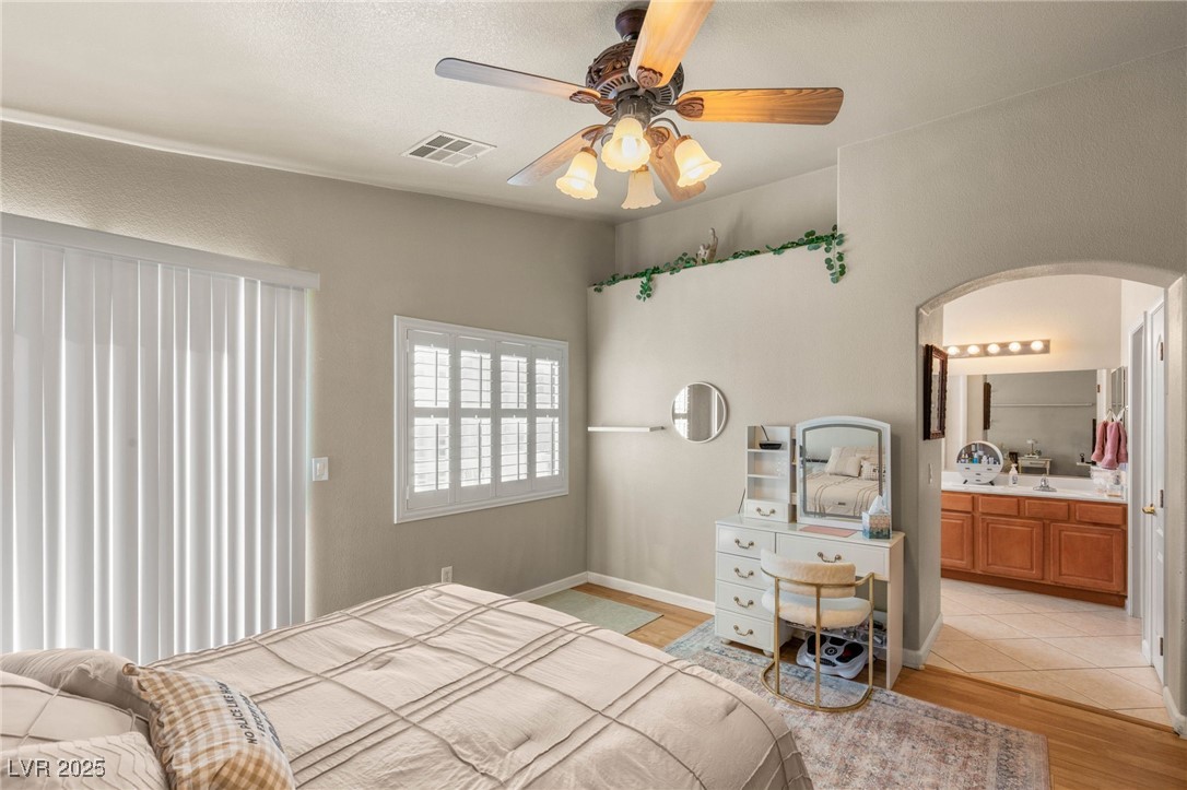 1591 Rusty Ridge Lane Henderson, NV 89002 - Photo 18 of 27 Bedroom featuring light wood-style flooring, ceiling fan, arched walkways, and ensuite bath
