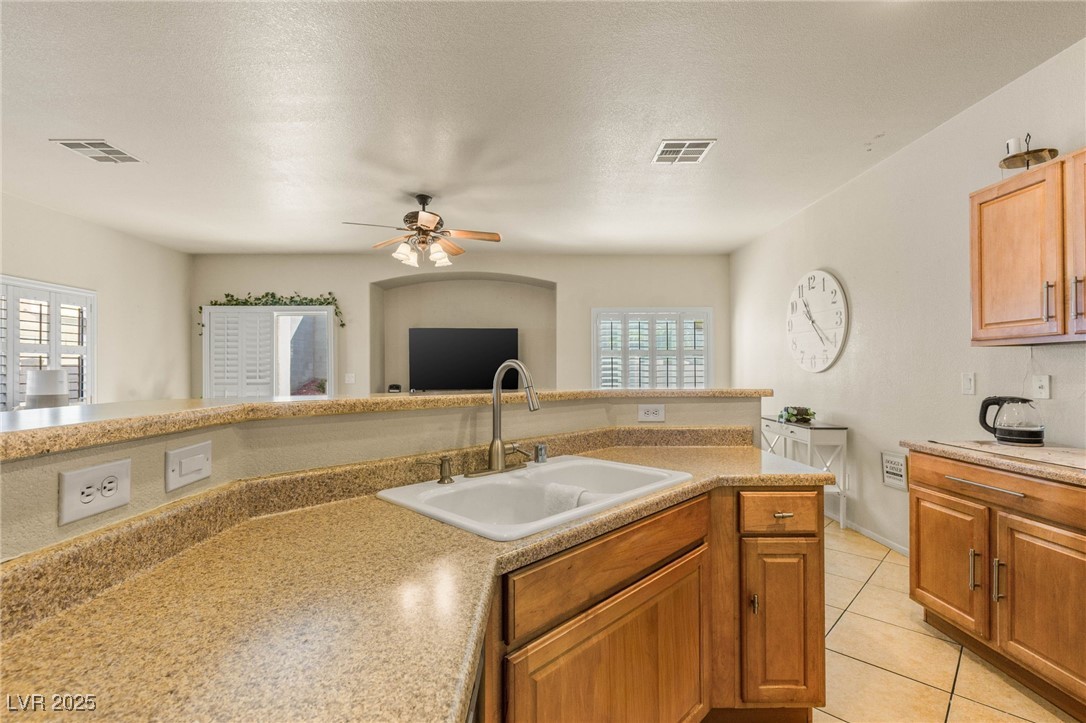 1591 Rusty Ridge Lane Henderson, NV 89002 - Photo 9 of 27 Kitchen with light tile patterned floors, a textured ceiling, brown cabinets, a ceiling fan, and light stone counters