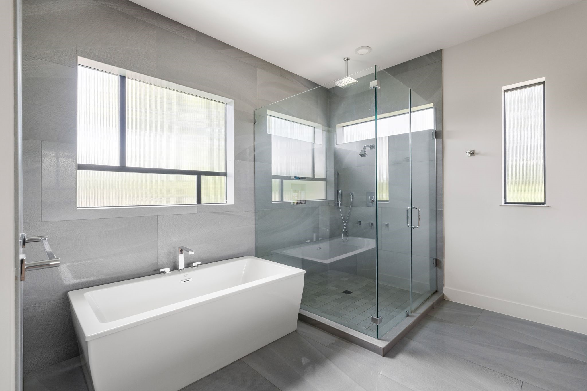 5427 Maple Street Houston, TX 77096 - Photo 25 of 46 The primary bath closes offers a true retreat: a freestanding soaking tub sits beneath a wide window, paired with a glass-enclosed walk-in shower finished in tonal stone tile with a ceiling-mounted rain shower-head.