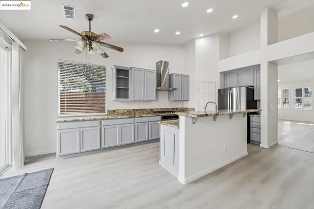 a large kitchen with stainless steel appliances kitchen island granite countertop a stove a sink a refrigerator and white cabinets with wooden floor