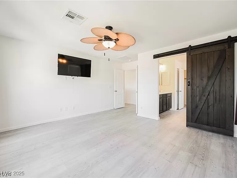 7600 Finishing Touch Court Las Vegas, NV 89149 - Photo 14 of 32 Unfurnished living room with light wood-style floors, a ceiling fan, and a barn door