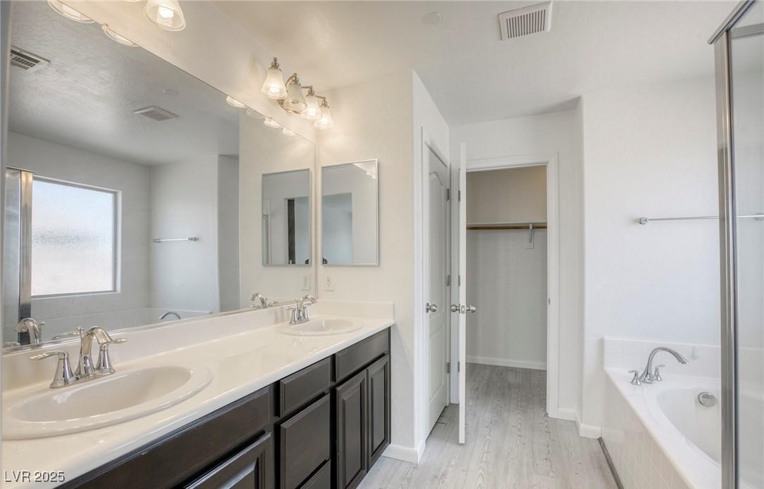 7600 Finishing Touch Court Las Vegas, NV 89149 - Photo 17 of 32 Bathroom with a bath, double vanity, a walk in closet, and light wood-style flooring