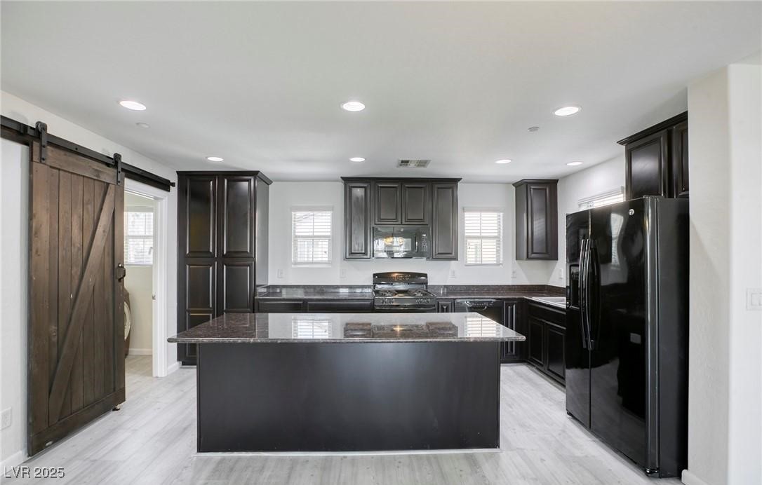 7600 Finishing Touch Court Las Vegas, NV 89149 - Photo 5 of 32 Kitchen with dark stone counters, black appliances, a center island, light wood-style floors, and recessed lighting