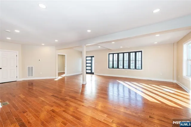 a view of an empty room with wooden floor and a kitchen
