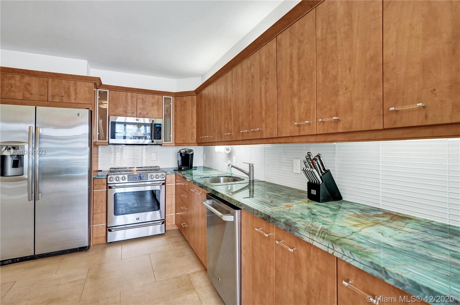 5750 Collins Avenue, Unit 15F Miami Beach, FL 33140 - Photo 13 of 65 a kitchen with stainless steel appliances granite countertop a sink a stove a refrigerator a washer and dryer with wooden cabinets