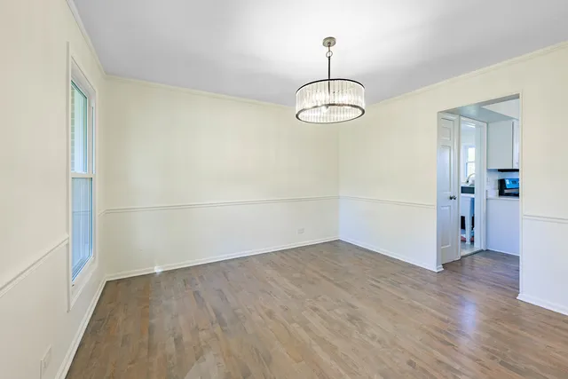an empty room with wooden floor and way to kitchen