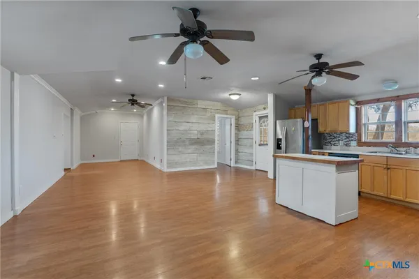 a view of an empty room and kitchen with ceiling fan wooden floor
