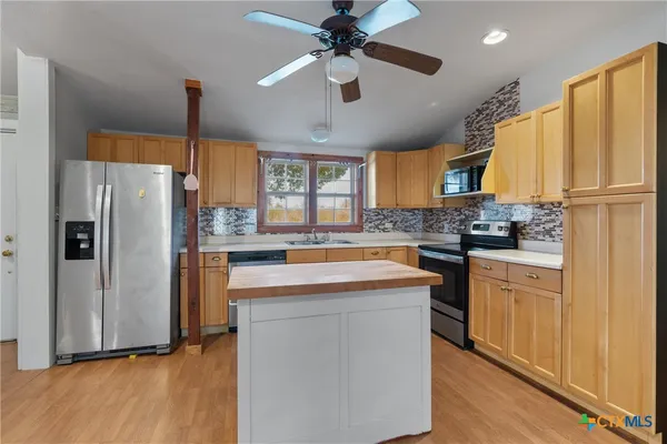 a kitchen with stainless steel appliances granite countertop a refrigerator a sink dishwasher a stove with white cabinets and wooden floor