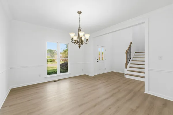 a view of an empty room with wooden floor kitchen view and a window