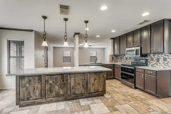 a large kitchen with kitchen island lots of wooden cabinets a sink a stove and a chandelier