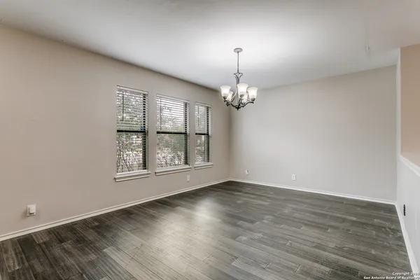an empty room with wooden floor chandelier and windows