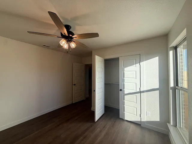 an empty room with wooden floor fan and windows