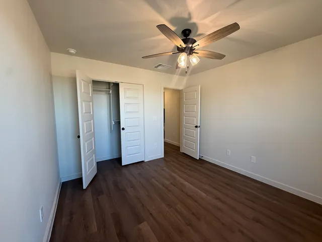 an empty room with wooden floor closet and fan